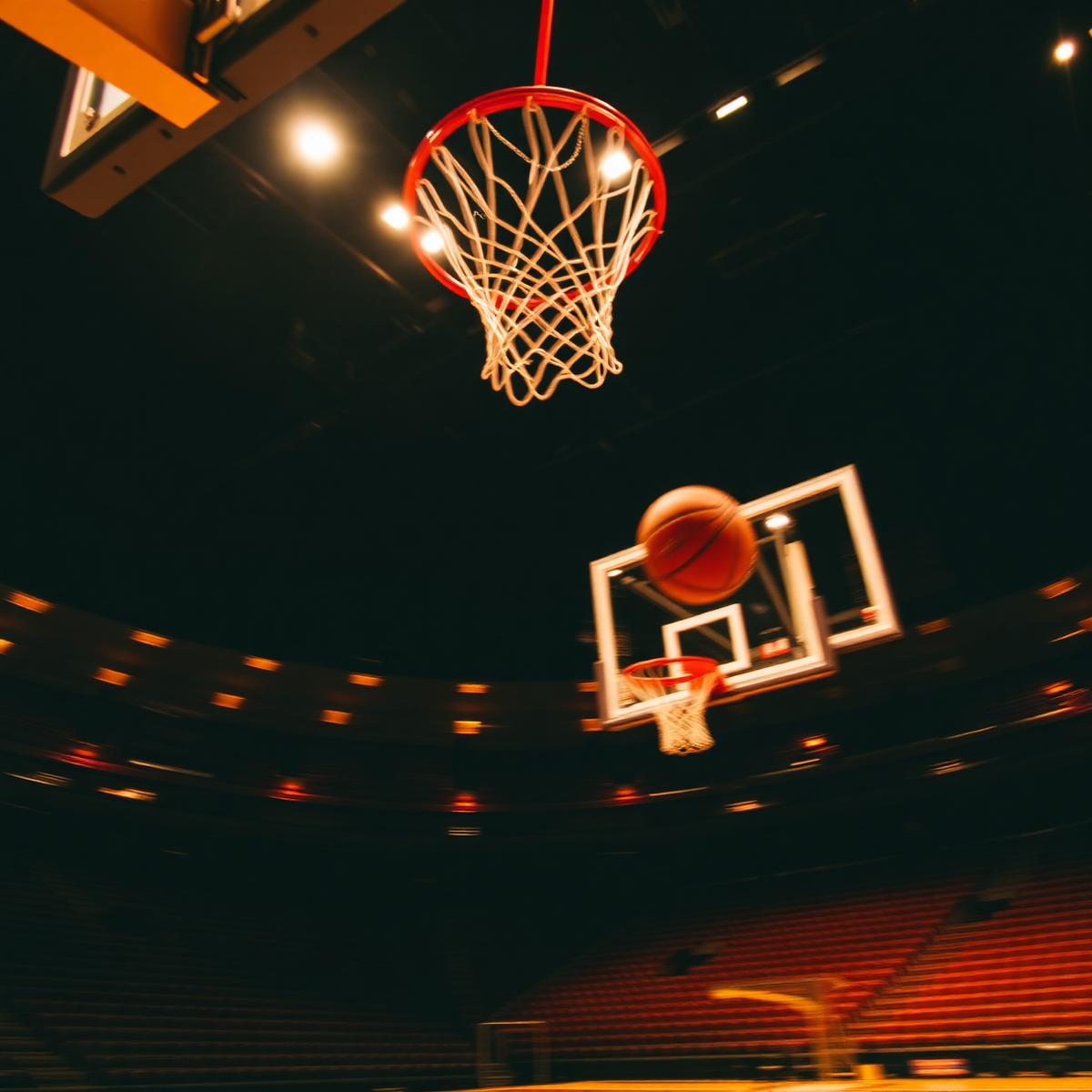 Basketball in flight toward the hoop in a floodlit arena